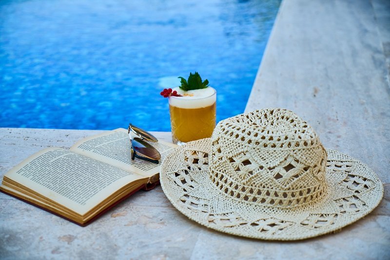 A Beige Straw Hat Book Sunglasses And Drink Beside A Pool Photo By Engin Akyurt From Pexels